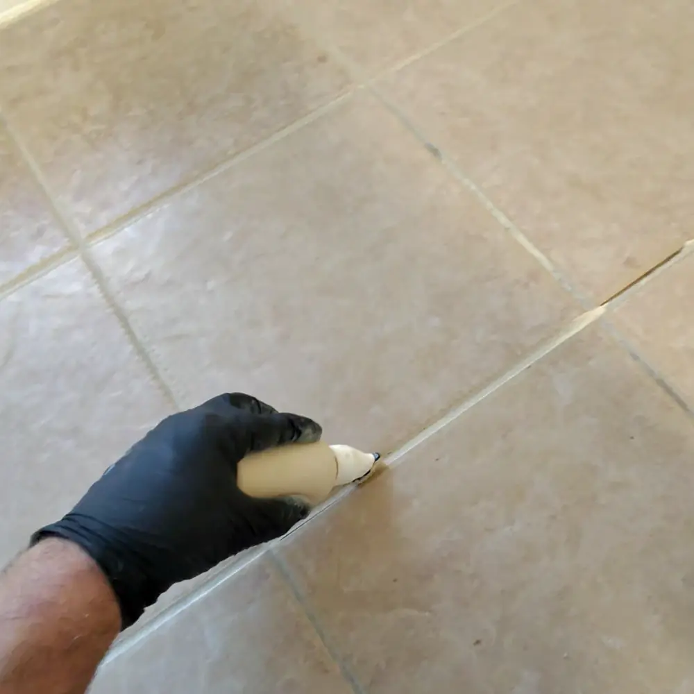 Hank's technician hand-applying grout color sealant along a grout line